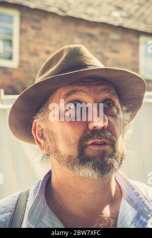 1940s man husband, in trilby hat, isolated outdoors in garden sunshine by vintage laundry looking up worried, 1940s wartime Britain event, UK. Stock Photo