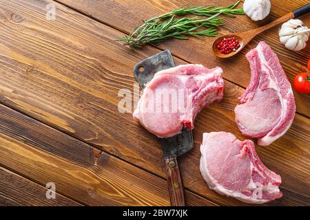 Raw pork meat chopes with herbs and spices with meat american cleaver on wooden background side view space for text. Diagonal. Stock Photo