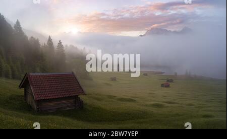 Perfect scenic sunrise in the Mountains - huts, lake, fog, colorful sky Stock Photo