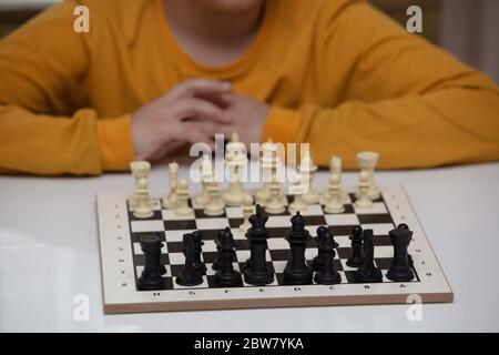 sits at a table and plays chess. The kid concentrated on the game  Stock Photo