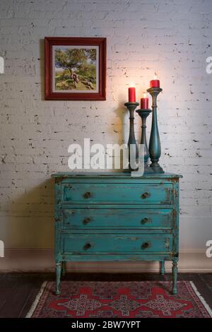 Retro composition of Green vintage cabinet, candlesticks with lighted candles and hanged painting on white bricks wall in studio Stock Photo