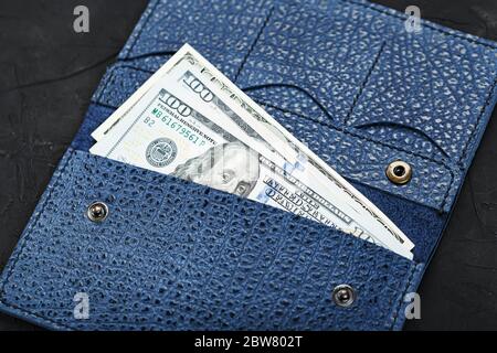 Purse of blue color from genuine leather with new one hundred dollar bills on a black background. Stock Photo