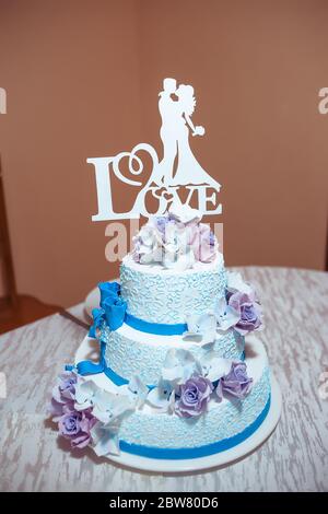 A beautiful blue wedding cake decorated with creamy white and purple flowers with the silhouette of a bride and groom. I love you inscription. Stock Photo