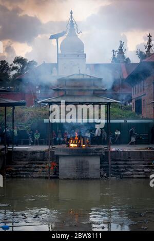 Relatives wait at a funeral pyre. Bagmati River, Arya Ghat, Pashupatinath temple. Kathmandu, Nepal, Nepalese, Asia, Asian, Himalayas. Stock Photo