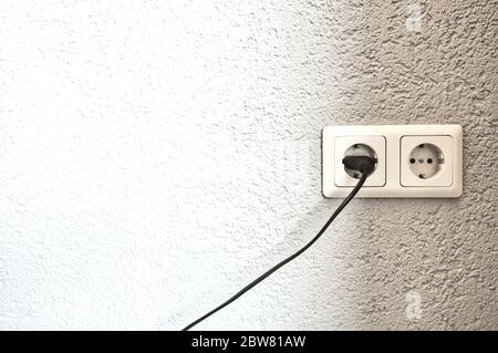 Double electrical power European socket with black cable and plug on white wall space for text Stock Photo
