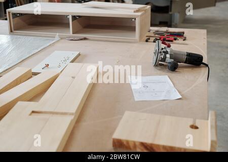 Workplace on contemporary furniture factory worker with group of wooden boards, electric handtool and sketch of workpiece Stock Photo