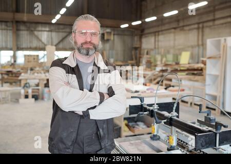 Successful senior master of contemporary furniture producing factory standing in front of camera with workshop interior on background Stock Photo