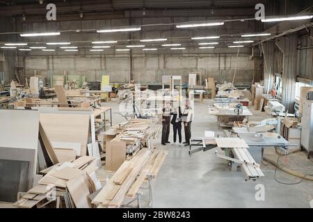 Group of workers of contemporary factory discussing furniture producing materials while sales manager pointing at them at meeting Stock Photo