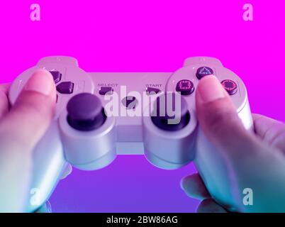Hands of a black woman holding a video game controller. Selective focus on a button. Blurry background. Pink and blue. Stock Photo