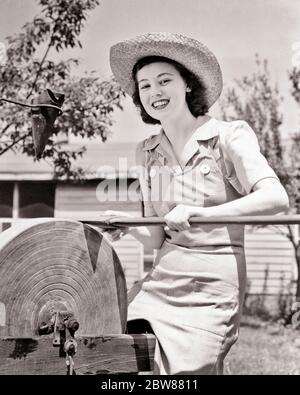 1940s SMILING YOUNG FARM WOMAN WEARING STRAW HAT LOOKING AT CAMERA WHILE SHARPENING LONG HANDLE AX ON SANDSTONE GRINDING WHEEL   - f3112 HAR001 HARS JUVENILE YOUNG ADULT COMIC SAFETY EDGE PLEASED JOY LIFESTYLE SATISFACTION FEMALES RURAL HEALTHINESS HOME LIFE COPY SPACE HALF-LENGTH LADIES PERSONS FARMING RISK CONFIDENCE AGRICULTURE B&W EYE CONTACT AXE GOALS HUMOROUS HAPPINESS CHEERFUL CHORE FARMERS LOW ANGLE COMICAL PRIDE SHARP SMILES CONNECTION COMEDY HANDLE JOYFUL TEENAGED AX COOPERATION HONE HONING JUVENILES SHARPENING TASK YOUNG ADULT WOMAN BLACK AND WHITE CAUCASIAN ETHNICITY GRINDING Stock Photo