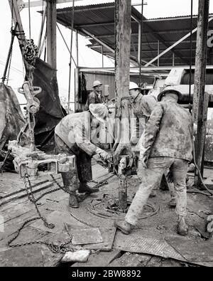 1960s FOUR MEN ROUGHNECKS DRILLERS WEARING SAFETY HARD HATS AND CANVAS CLOTHING WORKING ON OFFSHORE OIL DRILL IN GULF OF MEXICO - i3161 HAR001 HARS SKILLS HIGH ANGLE DANGEROUS DRILLING MANUAL STRENGTH CAREERS LABOR RISKY EMPLOYMENT HAZARDOUS OCCUPATIONS OFFSHORE PERIL UNSAFE CONCEPTUAL GULF OF MEXICO SUPPORT EMPLOYEE JEOPARDY TRADE COOPERATION MID-ADULT MID-ADULT MAN PETROLEUM YOUNG ADULT MAN BLACK AND WHITE CAUCASIAN ETHNICITY FOSSIL FUEL HAR001 LABORING OLD FASHIONED Stock Photo