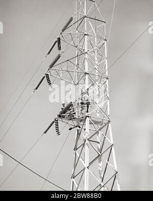 1960s TWO ANONYMOUS LINEMEN WORKING HIGH UP ON A METAL ELECTRIC POWER UTILITY TRANSMISSION TOWER INSTALLING A ROW OF INSULATORS  - i4404 HAR001 HARS CUSTOMER SERVICE CAREERS LOW ANGLE POWERFUL LABOR A OF ON UP EMPLOYMENT OCCUPATIONS TRANSMISSION UTILITY ANONYMOUS EMPLOYEE TRADE LINEMEN TOGETHERNESS BLACK AND WHITE GRID HAR001 INSTALLING LABORING OLD FASHIONED PUBLIC UTILITY UTILITIES Stock Photo