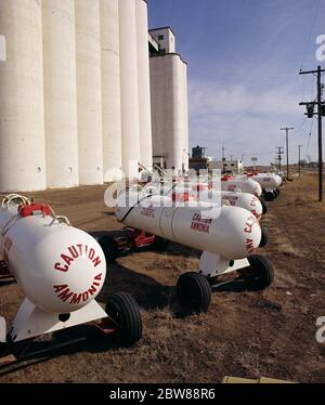 1980s FARMERS COOP WHITE GRAIN SILOS RED AND WHITE TANKS OF ANHYDROUS AMMONIA FOREGROUND CAUTION AMMONIA SIGN KANSAS USA - kf17798 HEL001 HARS GROWTH FOREGROUND GREAT PLAINS OLD FASHIONED Stock Photo