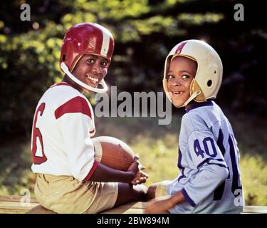 1970s TWO SMILING AFRICAN-AMERICAN BOYS SMILING LOOKING AT CAMERA OVER SHOULDERS WEARING FOOTBALL JERSEYS HELMETS HOLDING BALL - kj5647 PHT001 HARS ATHLETE PLEASED JOY LIFESTYLE BROTHERS HEALTHINESS HOME LIFE COPY SPACE FRIENDSHIP HALF-LENGTH MALES RISK ATHLETIC SIBLINGS CONFIDENCE EXPRESSIONS EYE CONTACT GOALS DREAMS HAPPINESS CHEERFUL PROTECTION AFRICAN-AMERICANS AFRICAN-AMERICAN RECREATION BLACK ETHNICITY PRIDE SIBLING SMILES CONNECTION JERSEYS JOYFUL HELMETS FOOTBALLS JUVENILES PRE-TEEN PRE-TEEN BOY TOGETHERNESS AMERICAN FOOTBALL OLD FASHIONED AFRICAN AMERICANS Stock Photo
