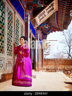 1970s WOMAN ENTERING PAINTED TEMPLE WEARING TRADITIONAL KOREAN DRESS CHIMA OR SKIRT WITH A SHORT JACKET OR JEOGORI SOUTH KOREA - kr18779 PHT001 HARS TEMPLE ORIENTAL STYLES ENTERING EXTERIOR A PAINTED KOREAN CULTURE STYLISH OR FASHIONS WORN YOUNG ADULT WOMAN INDIGENOUS OLD FASHIONED Stock Photo
