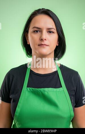 Female cook with green apron and black t-shirt, isolated on green background Stock Photo