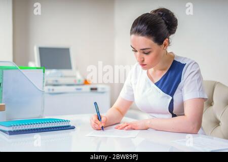 Female young doctor writing something sitting at her office. Healthcare and medical concept Stock Photo
