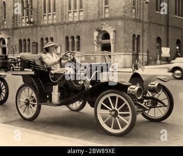 1940s ANONYMOUS WOMAN SITTING DRIVING AN ANTIQUE CAR ABOUT 1910 SMALL AMERICAN FLAGS DISPLAYED ON THE HOOD PERHAPS FOR A PARADE - m5756 HAR001 HARS AUTOMOBILES VEHICLES ANONYMOUS 1910 MID-ADULT PERHAPS BLACK AND WHITE CAUCASIAN ETHNICITY DISPLAYED HAR001 OLD FASHIONED Stock Photo