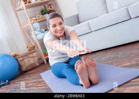 Healthy Lifestyle. Young woman doing yoga at home sitting legs apart bending down stretching smiling joyful Stock Photo