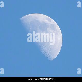 Daytime moon against bright blue sky Stock Photo
