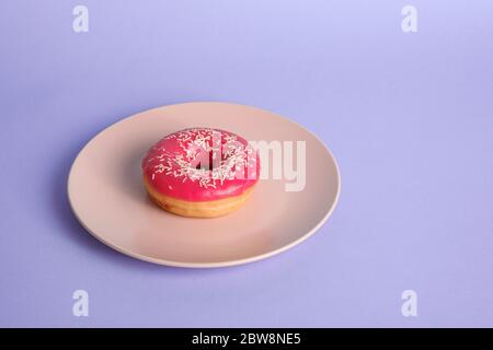 Pink red donut with white sprinkles on pink plate, sweet glazed dessert food on blue minimal background, angle view Stock Photo