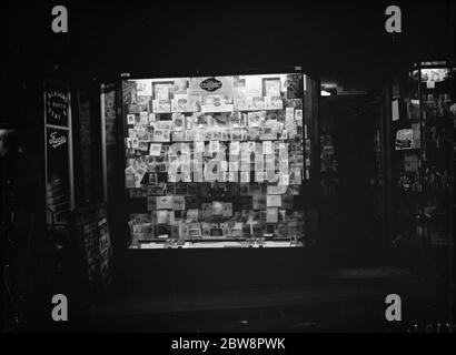 Shop window display of personalised Christmas greetings cards at Glen ' s library , lit up in Farningham , Kent . 1937 Stock Photo