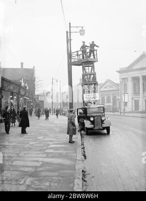Workers from the Demolition and Construction Company Ltd use their Bedford Tram Tower truck to work on the overhead street lights . 1936 . Stock Photo