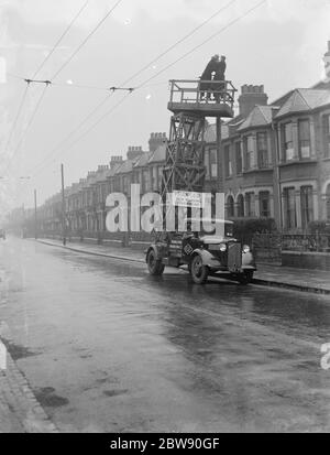 Workers from the Demolition and Construction Company Ltd use their Bedford Tram Tower truck to work on the overhead electrical trolleybus wires . 1937 . Stock Photo