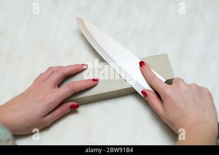 lonely woman sharpening a knife on a grindstone in the kitchen, man's work Stock Photo