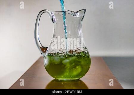blue liquid being poured into green liquid in a clear glass pitcher Stock Photo