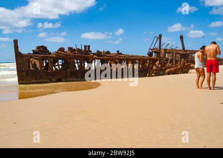 Fraser Island Australia - March 13 2014; Two tourists on beach by  Maheno shipwreck rusting away on beach under blue sky. Stock Photo