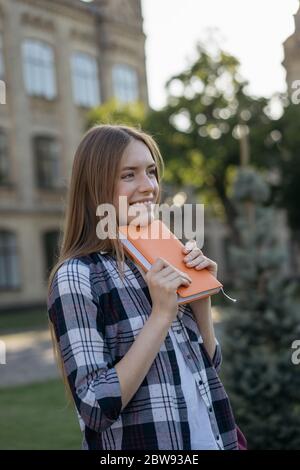 Student with backpack and book walking at home after good exam results. Education concept. Portrait of happy beautiful woman standing in park