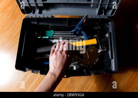 female hand with red manicure reaches for tools in an open tool box, view from the top Stock Photo