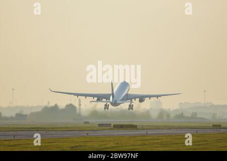 Wide-body passenger airliner taking off on sunset above the runway, back view, copy space. Plane fly up, yellow sky on background, soft focus. Vacatio Stock Photo