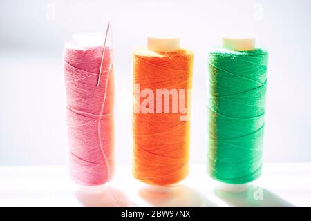 Three spools of thread and a needle on a white bright table, side view Stock Photo