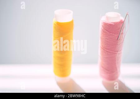 Yellow and pink spools of threads and a needle on a white bright table, side view Stock Photo