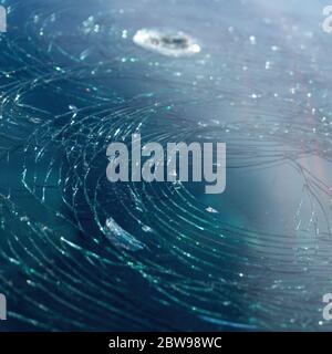 background of blue car broken windshield covered with circles of cracks. Hole on windscreen. Stock Photo