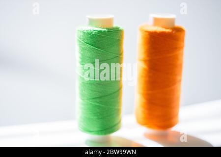 Green and orange spools of thread on a white table, side view Stock Photo