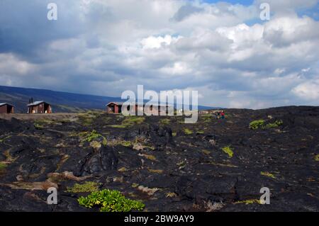 Vog and clouds cover blue sky over the Hawaii Volcanoes National Park.  Crusted lava field and ranger station sit at the end of Chain of Craters Road Stock Photo