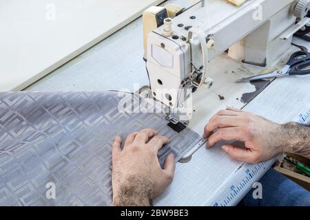 Tailor stitched seat fabrics. Close-up on man working with her sewing machine stitching a long length of fabric. Stock Photo