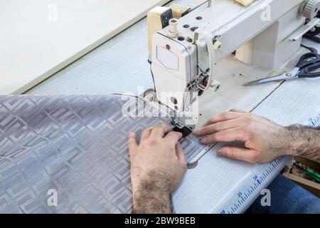 Tailor stitched seat fabrics. Close-up on man working with her sewing machine stitching a long length of fabric. Stock Photo