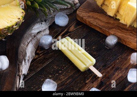 Pineapple, ice lollies and ice cubes over a wooden board Stock Photo