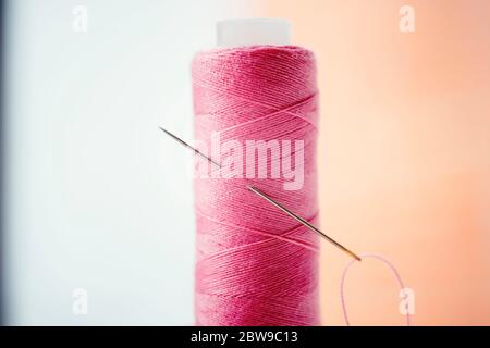 Pink spool of thread and a needle in it, side view, macro photo. Stock Photo