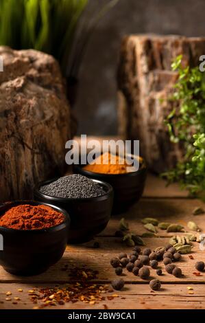 Three black small bowls with curry, poppy seeds and sweet paprika on a wooden table Stock Photo