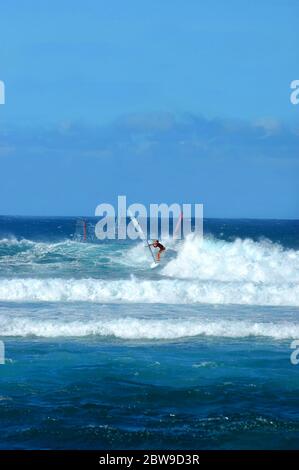 Boarder clings to his sailboard while windsurfing off the shores of Kauai, Hawaii.  Vivid blue water and swelling waves surround him. Stock Photo