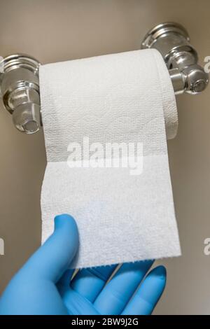 Close-up of hand in blue latex glove reaching for toilet paper Stock Photo