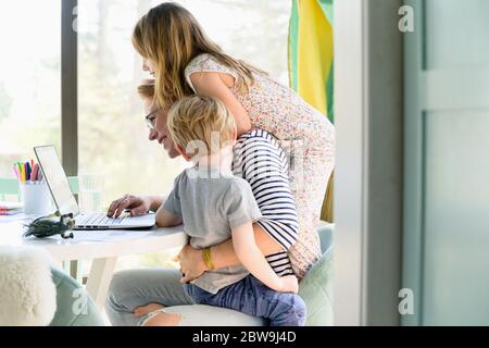 Children (4-5, 6-7) climbing on their mother while she works from home Stock Photo