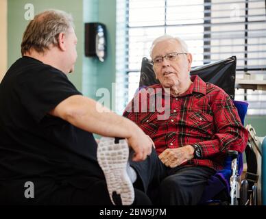 Senior man in wheelchair stretching leg on friends lap Stock Photo