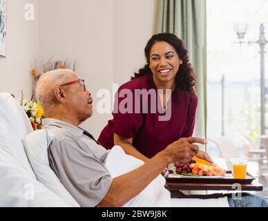 Nurse bringing healthy meal to senior man in bed Stock Photo