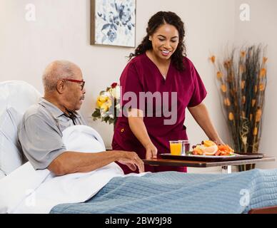 Nurse bringing healthy meal to senior man in bed Stock Photo